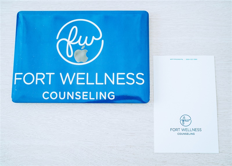 A laptop with the Fort Wellness Counseling logo on it and a notecard that says Fort Wellness Counseling