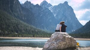 A couple sitting on a rock with mountains in the background.